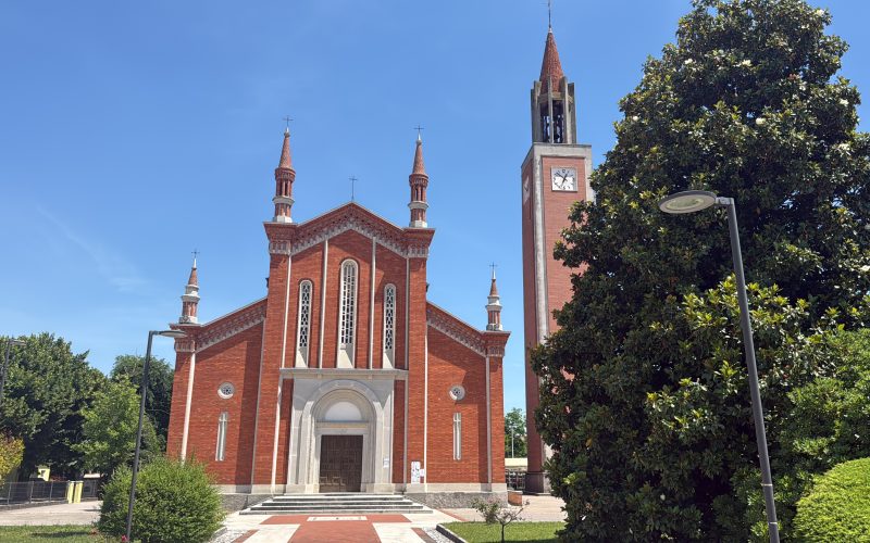 Facciata di chiesa color pesca con portone in legno e storico campanile separato in mattoni rossi con orologio a San Vito al Tagliamento.