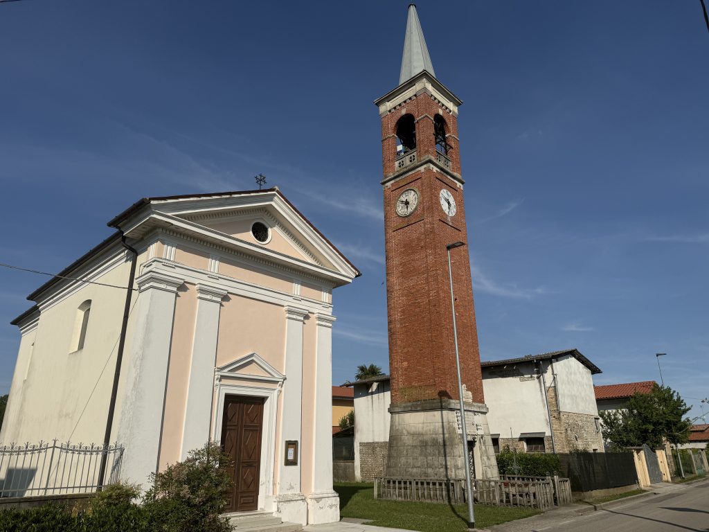 Imponente chiesa in mattoni rossi con pinnacoli decorativi e alto campanile a torre, circondata dal verde a Carbona.